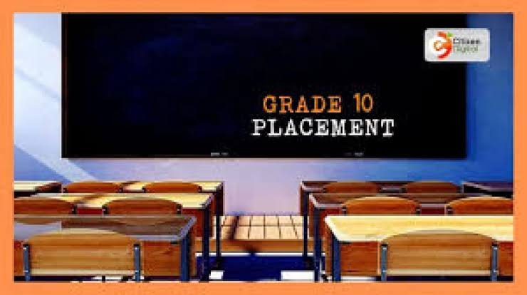A view of a standard Kenyan classroom with wooden desks and a chalkboard displaying Grade 10 placement information.