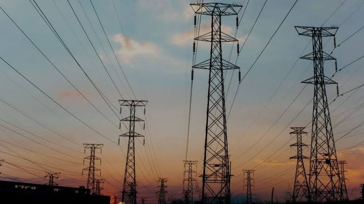 Silhouette of electricity transmission towers and power lines at a substation during sunset.