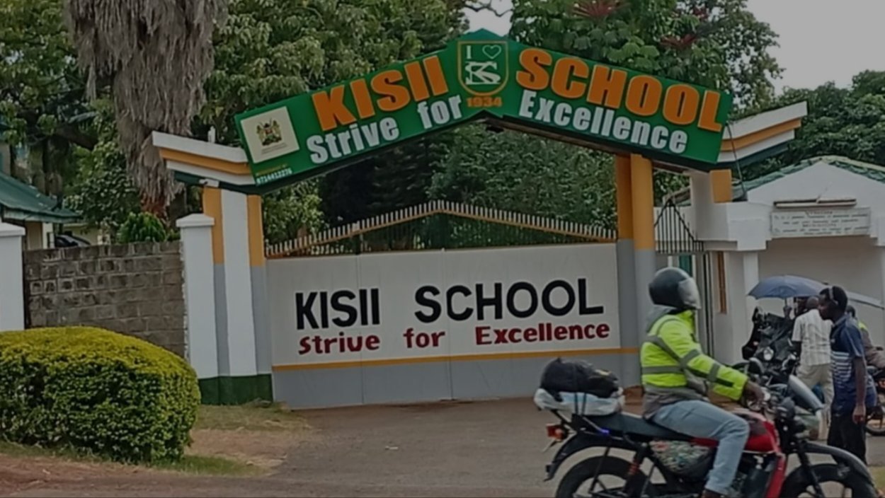 A view of the main entrance gate of Kisii School in Kenya with a motorcycle parked in front.