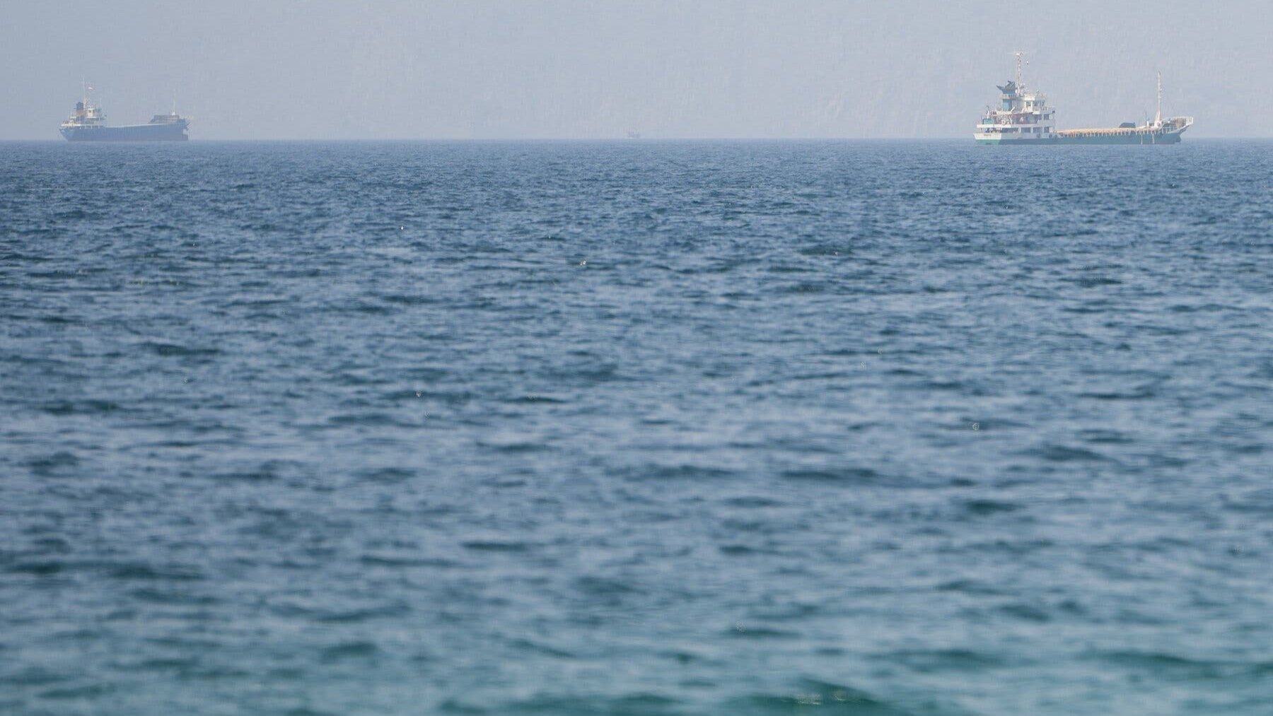Commercial cargo ships and oil tankers anchored in open ocean waters near the Strait of Hormuz.