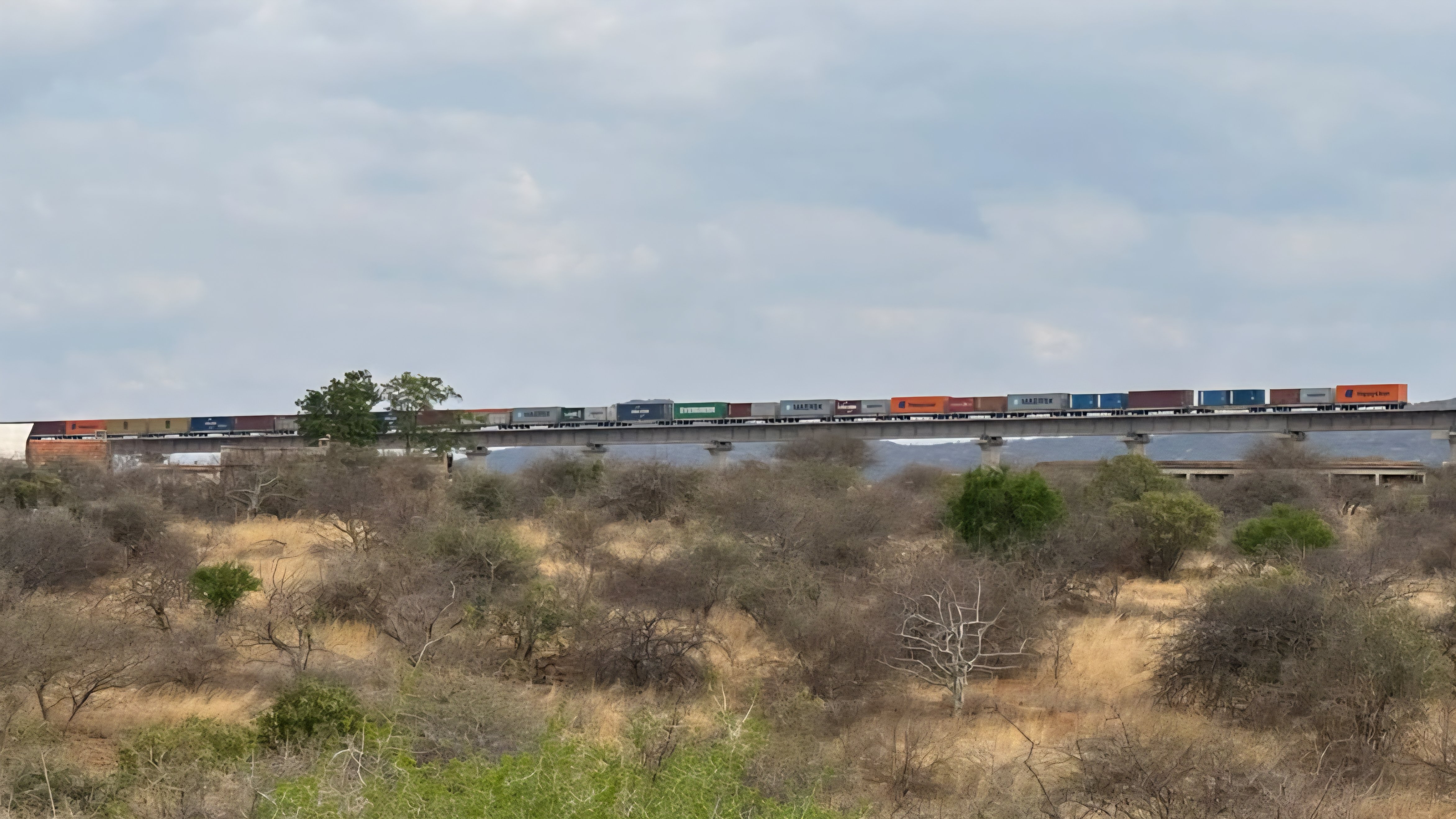 Two side-by-side photographs showing the modern railway infrastructure cutting across the dry shrublands of Tsavo under a partly cloudy sky.