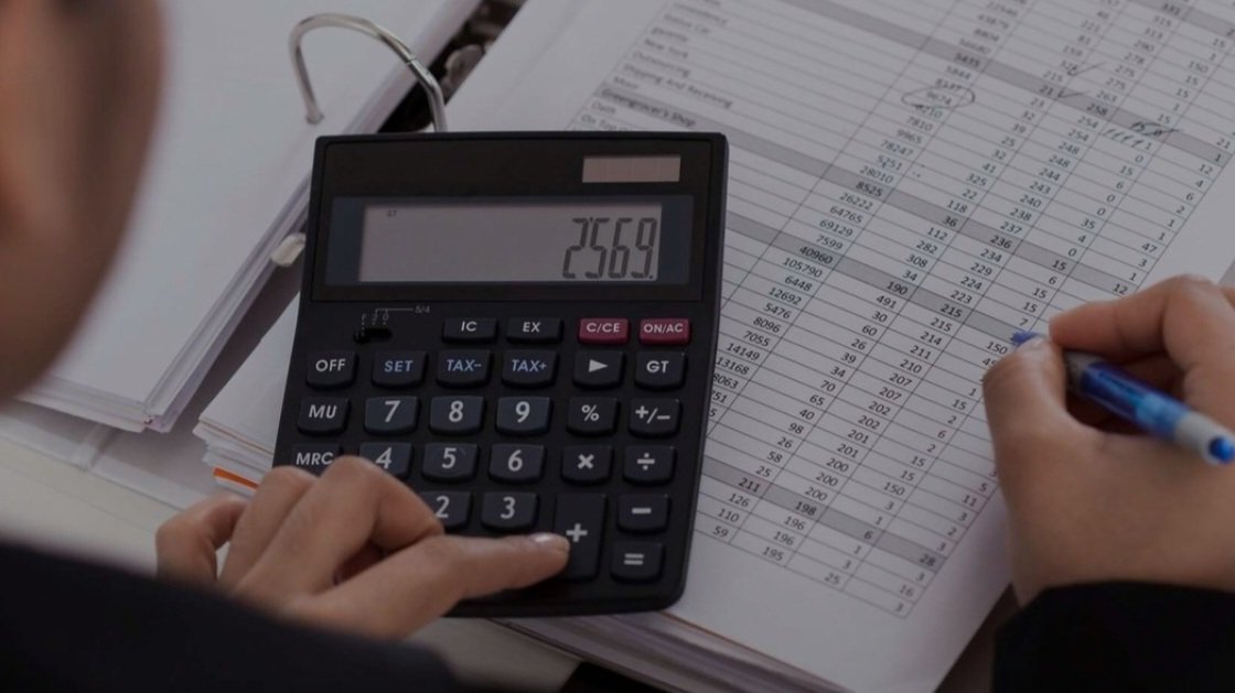 Close-up view of an office worker using a calculator over financial spreadsheets and corporate balance sheets.