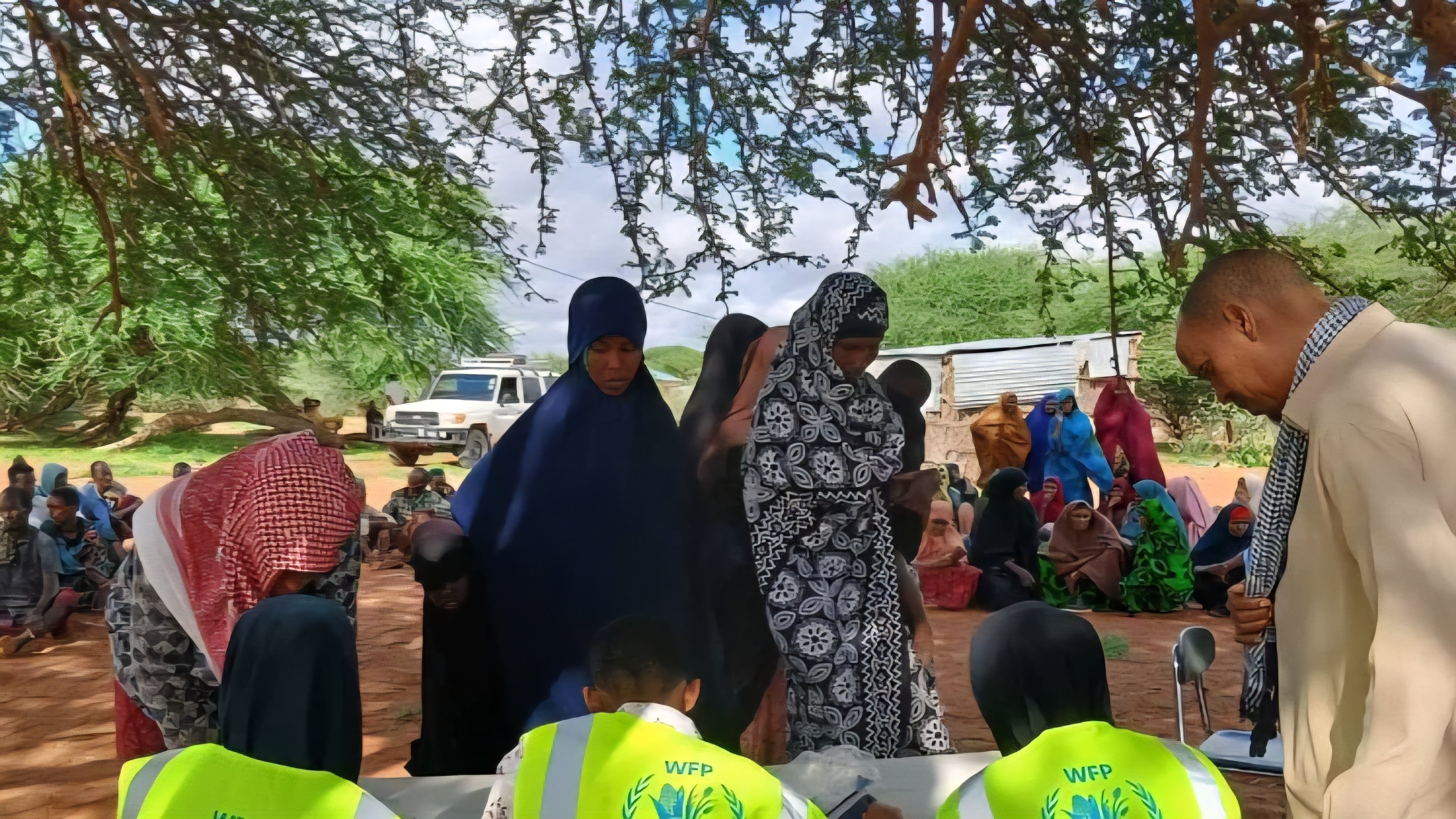 World Food Programme staff members wearing yellow vests sit at an outdoor field table in a rural location.