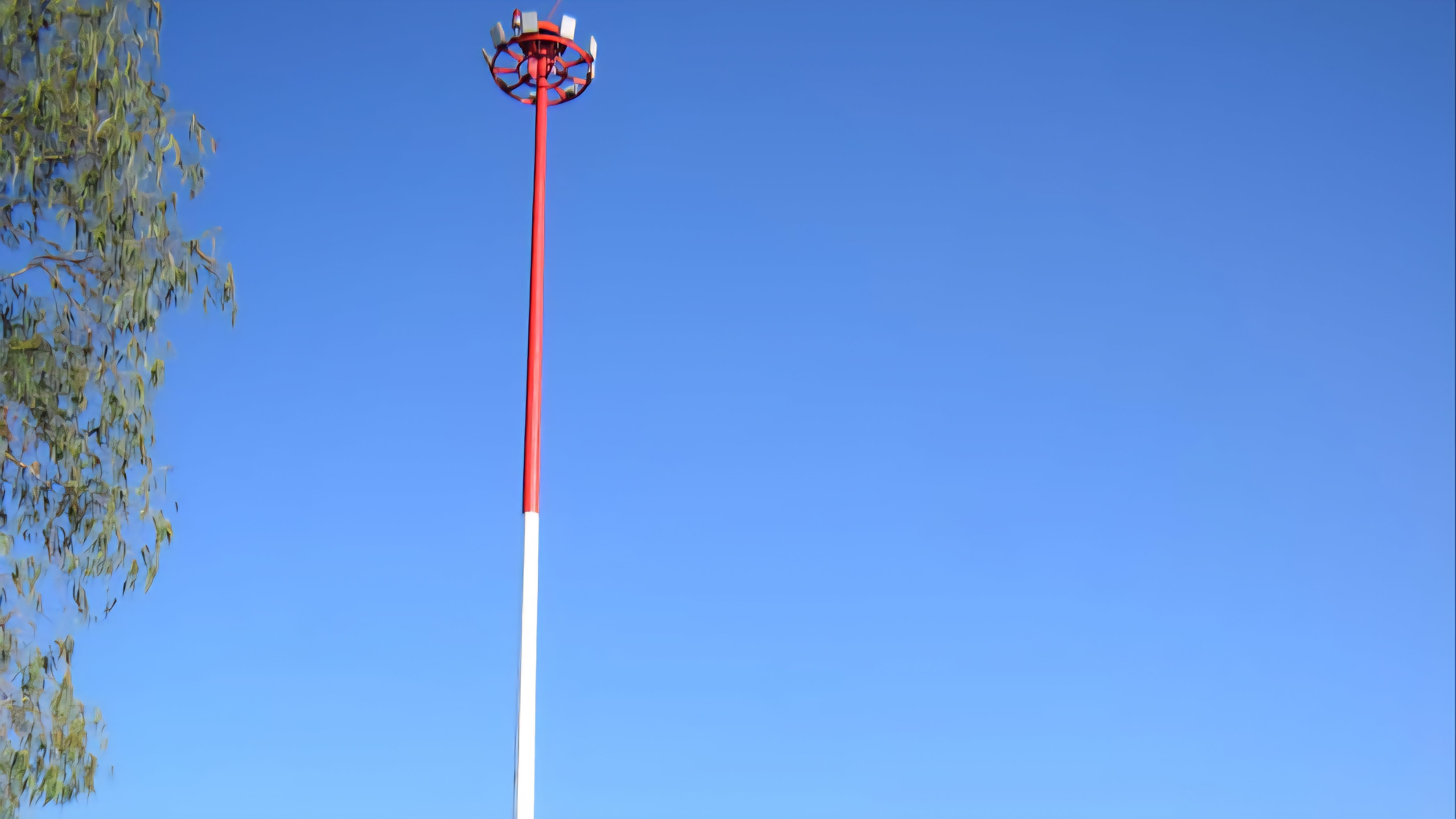 A tall red and white high mast lighting pole stands against a clear blue sky at Asembo Bay during a commissioning event.