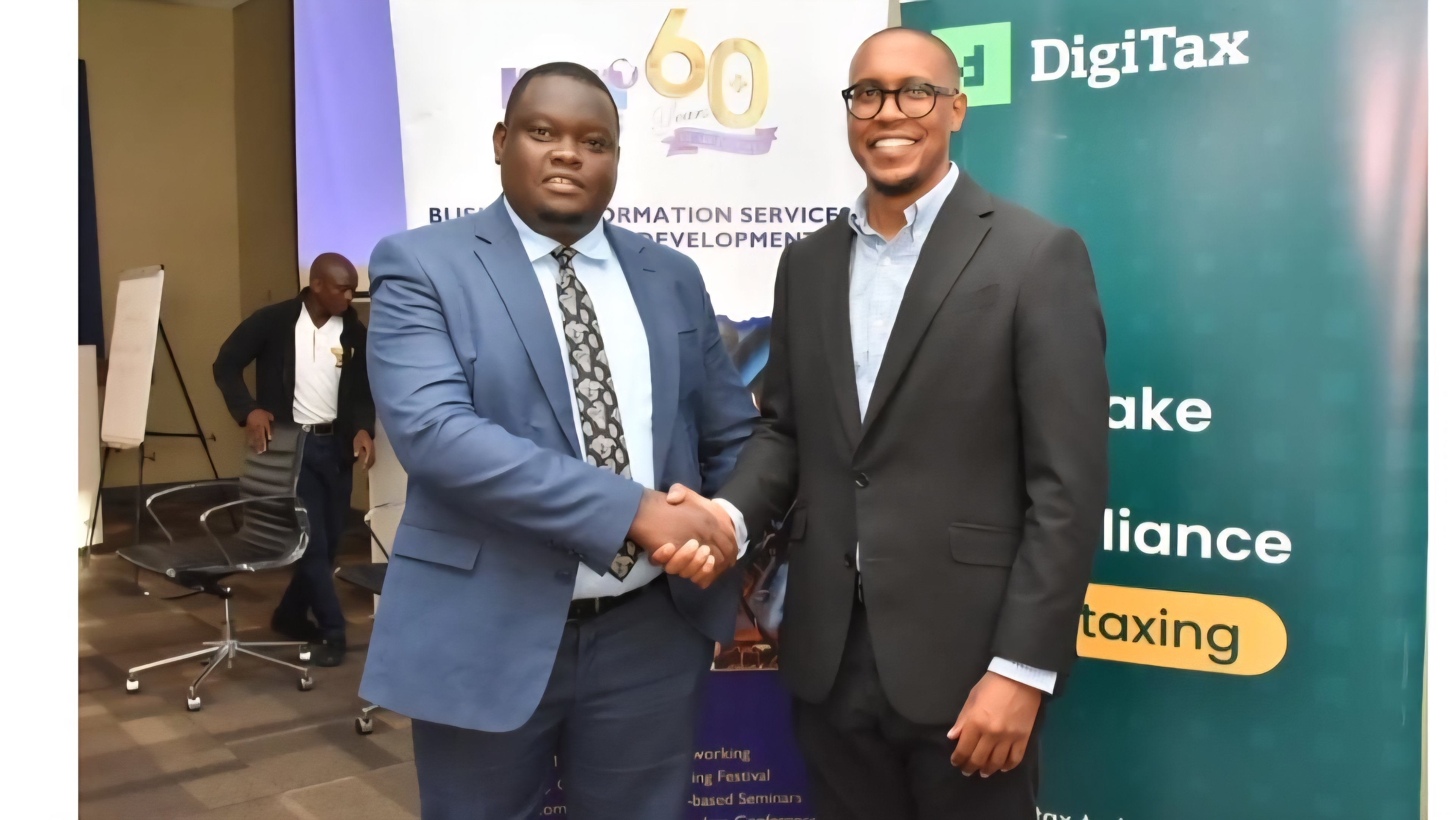 Two men in professional attire shaking hands in front of a backdrop featuring the DigiTax logo and information service branding.