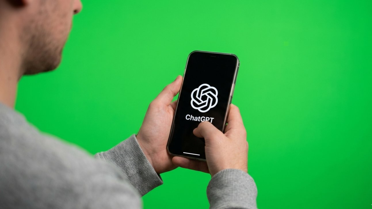 A person holding a smartphone displaying the ChatGPT logo on a green screen.