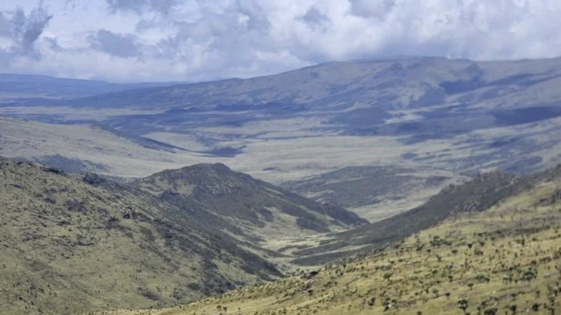 An aerial landscape photo showing the vast green valley and steep mountain ridges of the Aberdare Range under cloudy skies.