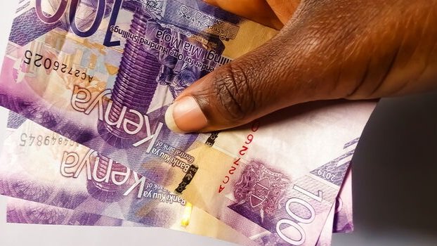 A close-up of Kenyan Shilling notes and US Dollar bills spread out on a wooden surface, representing the exchange rate volatility.