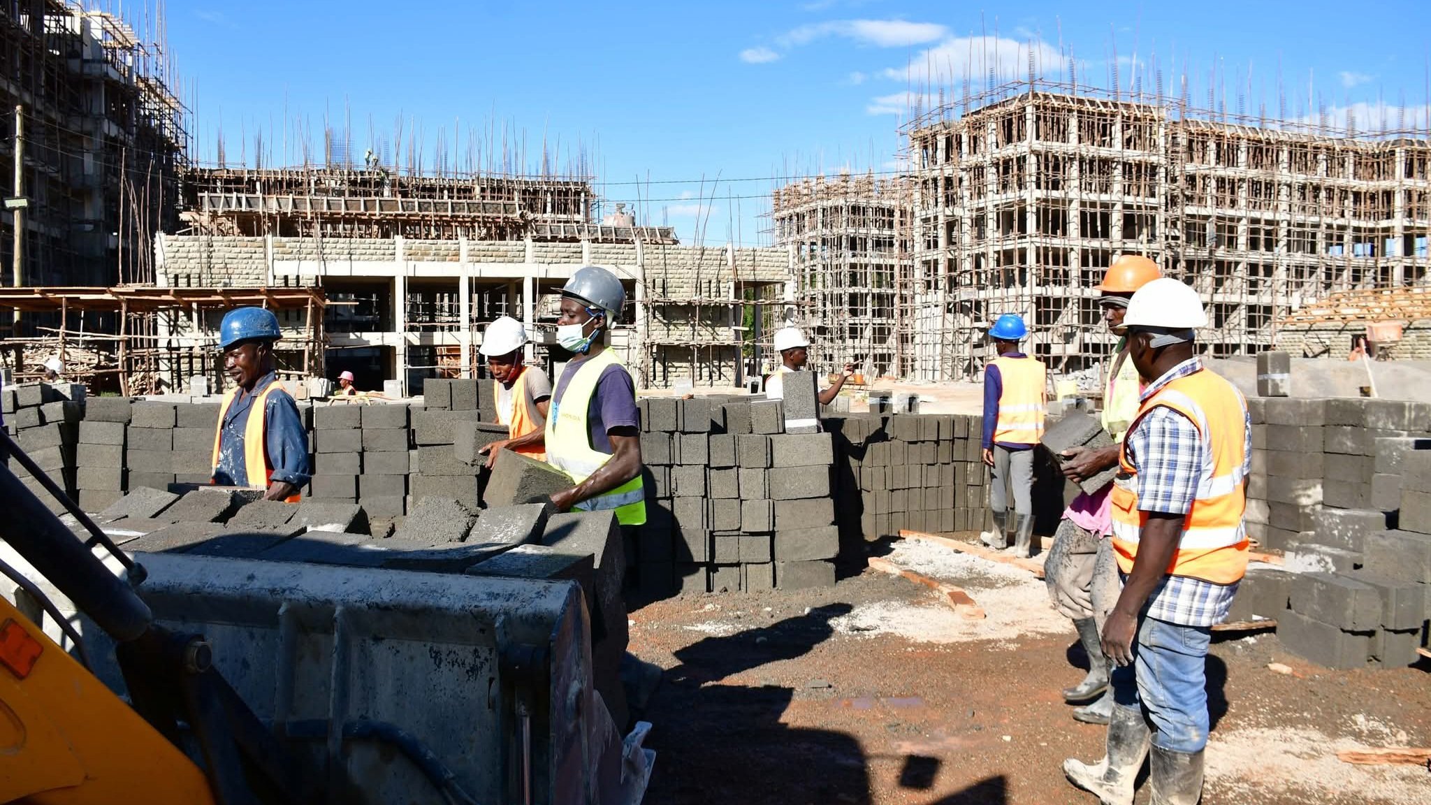 A wide-angle view of a multi-storey residential construction site in Bungoma with scaffolding and workers visible on a concrete block structure.