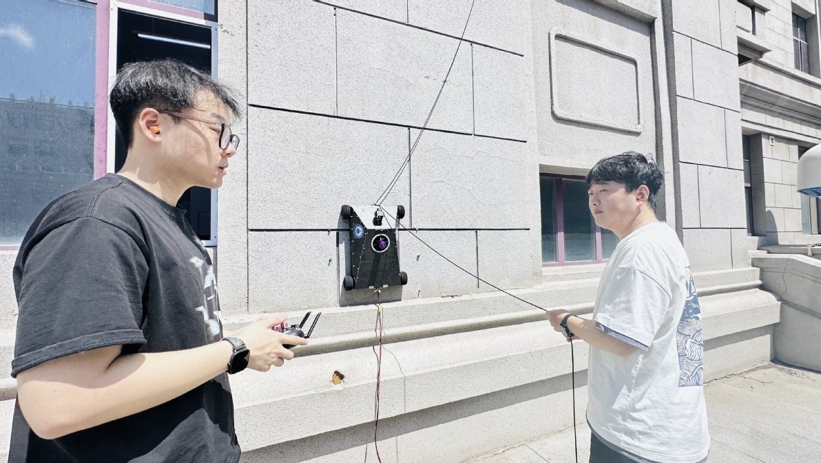 Research team members from Harbin Engineering University operating a wall-climbing robot on a smooth vertical surface during testing.