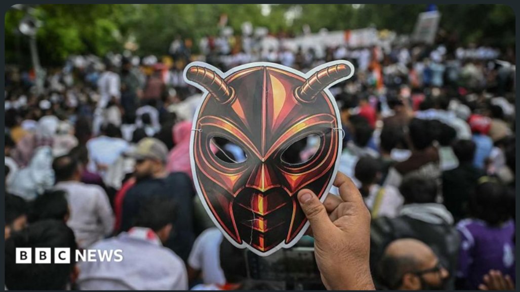 Demonstrators holding protest signs and a mask in New Delhi during youth-led education protests.