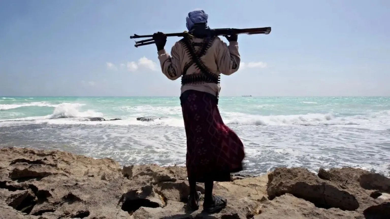 An armed man stands on a rocky Somali beach looking out toward the Indian Ocean where an oil tanker was recently hijacked.