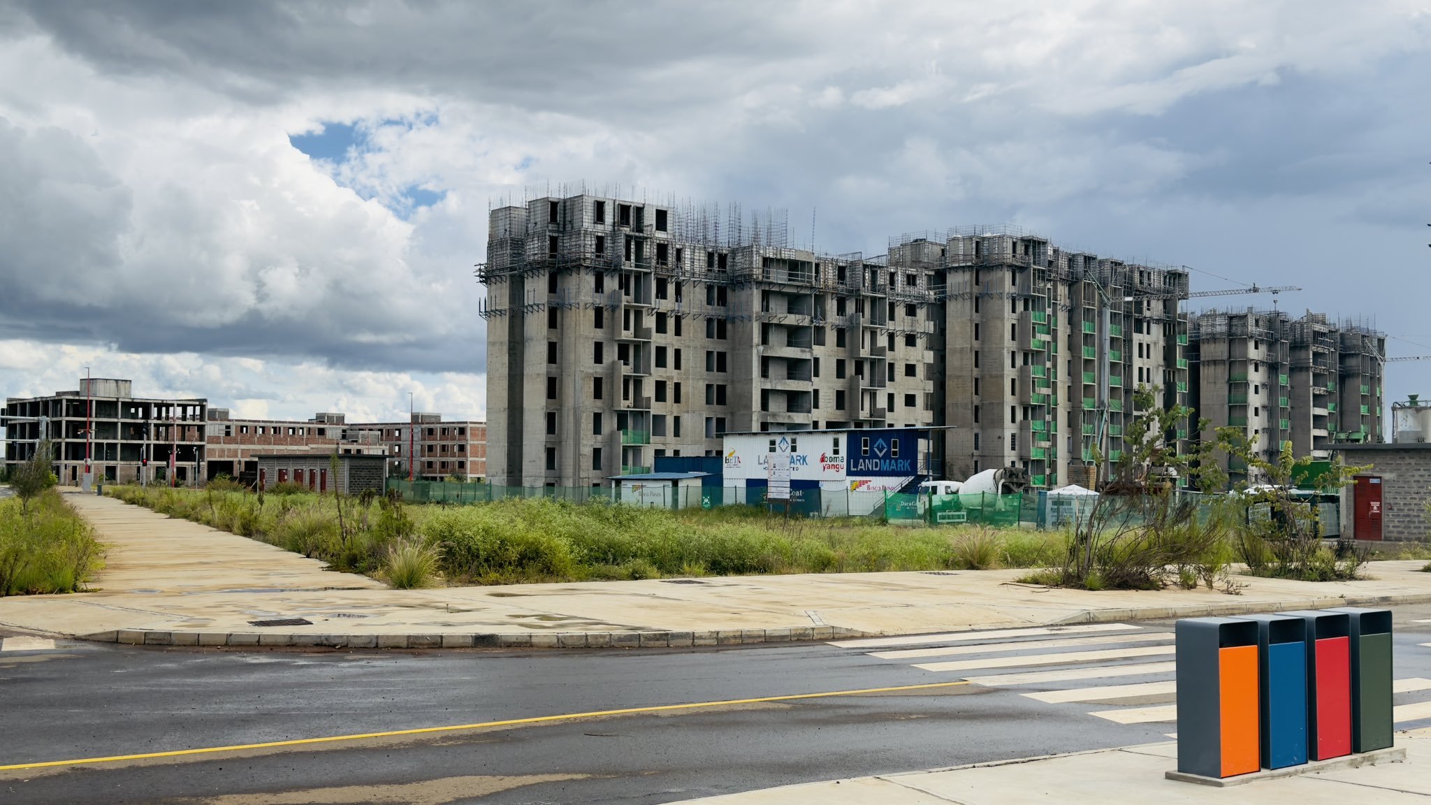Four multi-storey concrete apartment blocks under construction at Konza Technopolis, showing structural frames and external masonry against a cloudy sky with paved roads in the foreground.