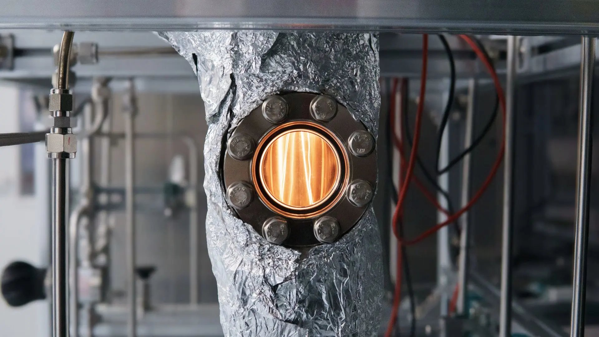 Close-up view of an illuminated metal filament glowing inside a sealed reactor flange assembly.