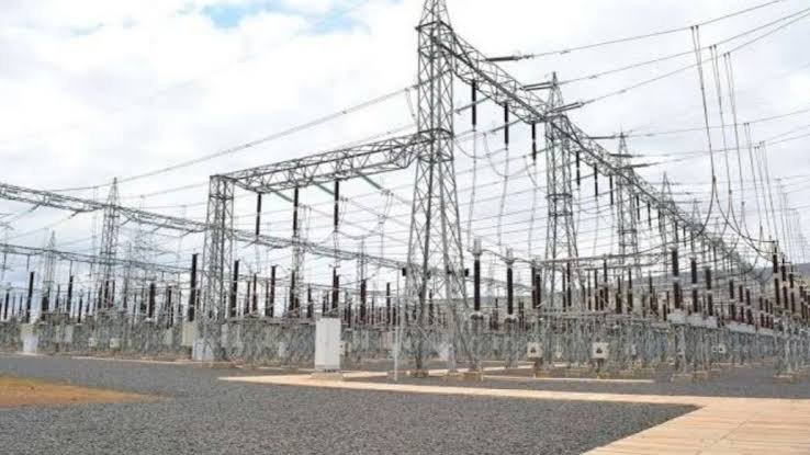 High-voltage power transmission towers and electrical lines running across a rural landscape under a clear sky.