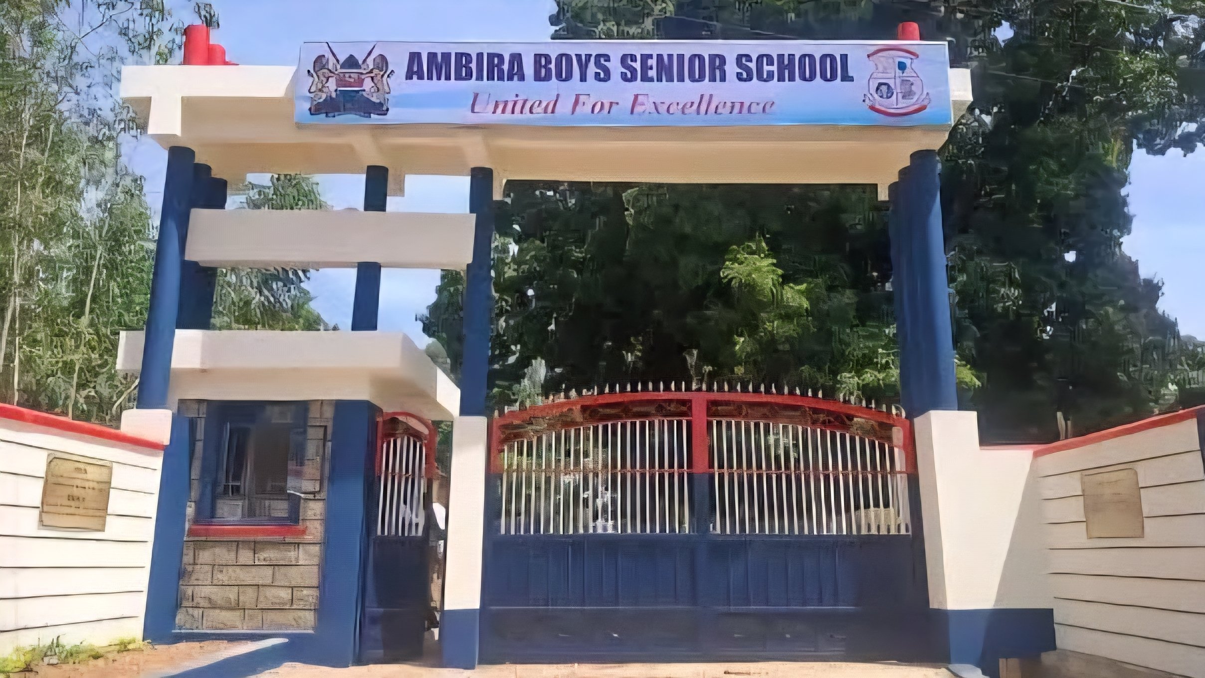 The main entrance gate of Ambira Boys Senior School with blue and white pillars and a red metal gate.