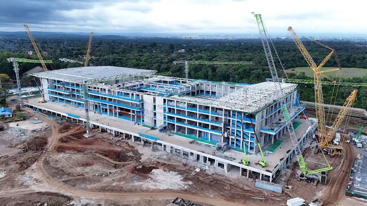Wide shot of the Bomas of Kenya main auditorium entrance showing construction scaffolding and renovation materials during a site inspection.