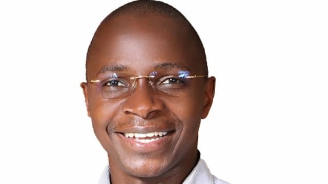 A portrait of a smiling man in a light-colored shirt and glasses against a white background.