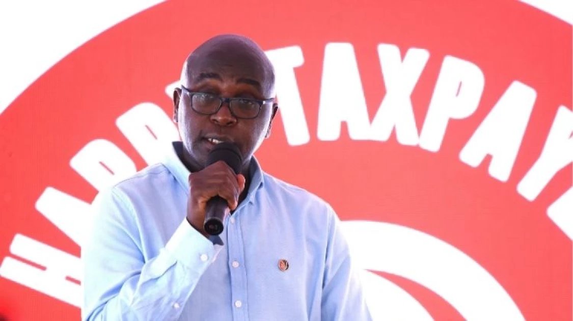 Former KRA Commissioner General Humphrey Wattanga speaking into a microphone during a public event with a taxpayer-themed backdrop.