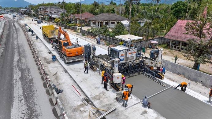 Aerial view of a large slipform paver machine laying fresh concrete during road construction in Germany.