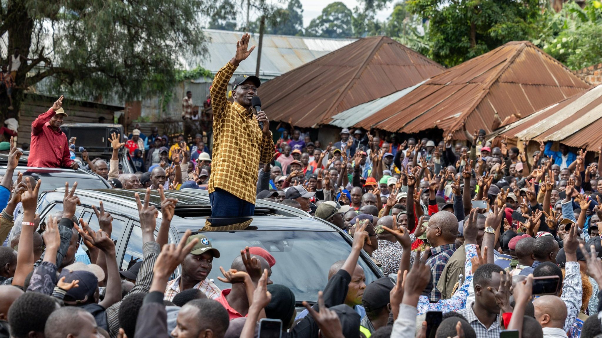 Photo of President William Ruto addressing a large, dense crowd from the sunroof of a vehicle in Nyamira County.