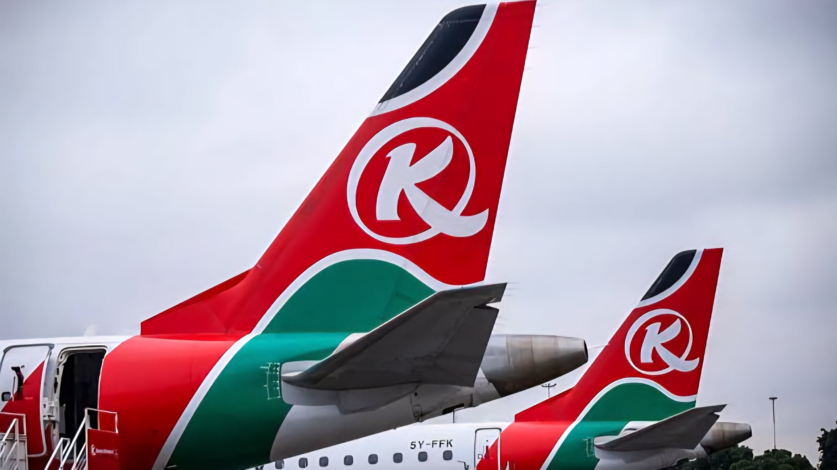The tail fin of a Kenya Airways Boeing 737-800 featuring the red 'K' logo parked on the apron at Jomo Kenyatta International Airport in Nairobi.