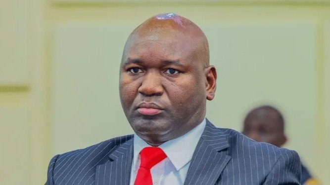 A professional portrait of Julius Bitok, the Principal Secretary for the State Department for Basic Education, wearing a suit and red tie.