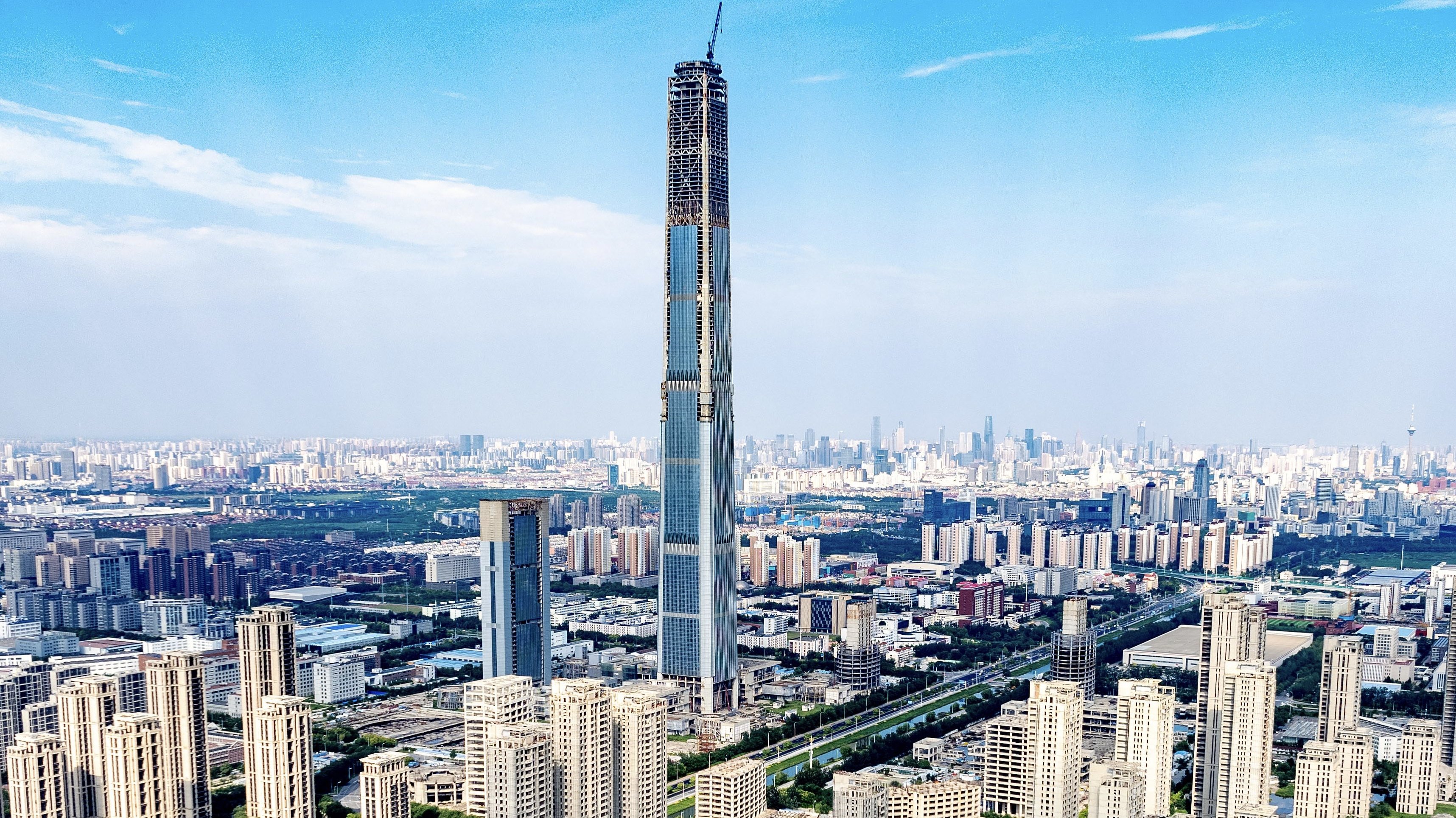 The partially completed Goldin Finance 117 skyscraper rising above the Tianjin skyline, its upper floors and unfinished crown visible against an overcast sky.