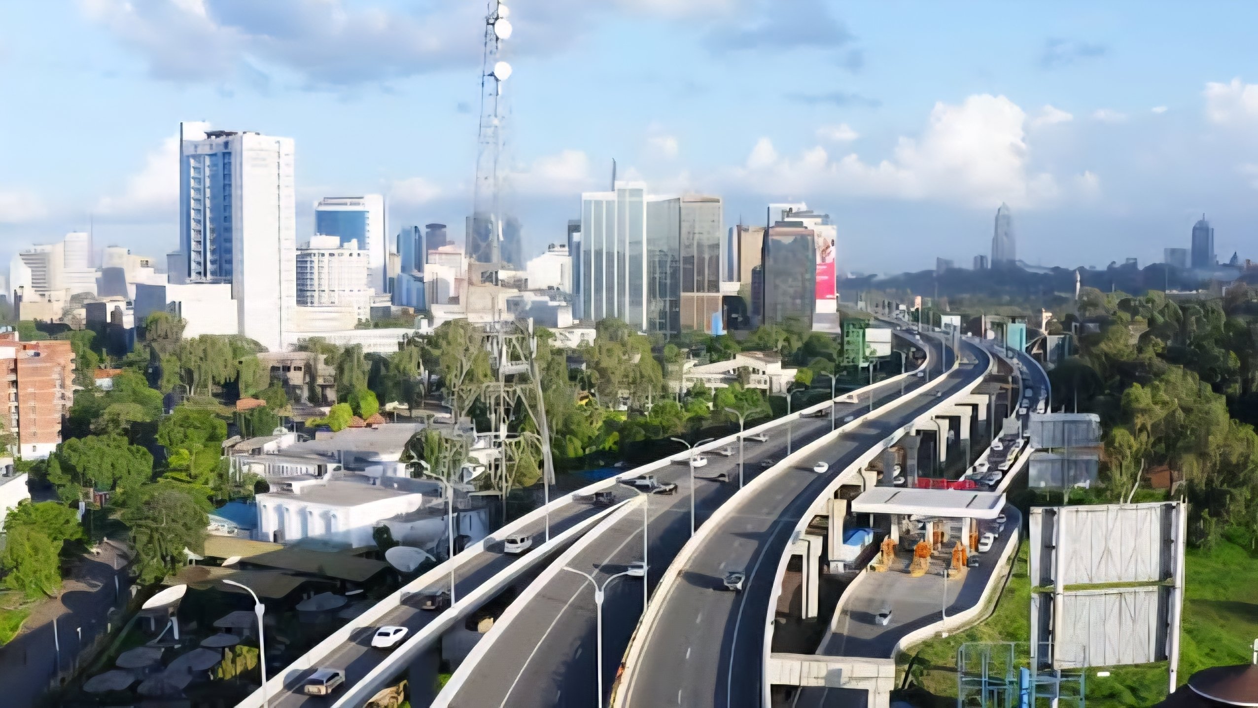 An aerial view of the Nairobi Expressway and city skyline, featuring high-rise buildings and modern road infrastructure under a clear sky.