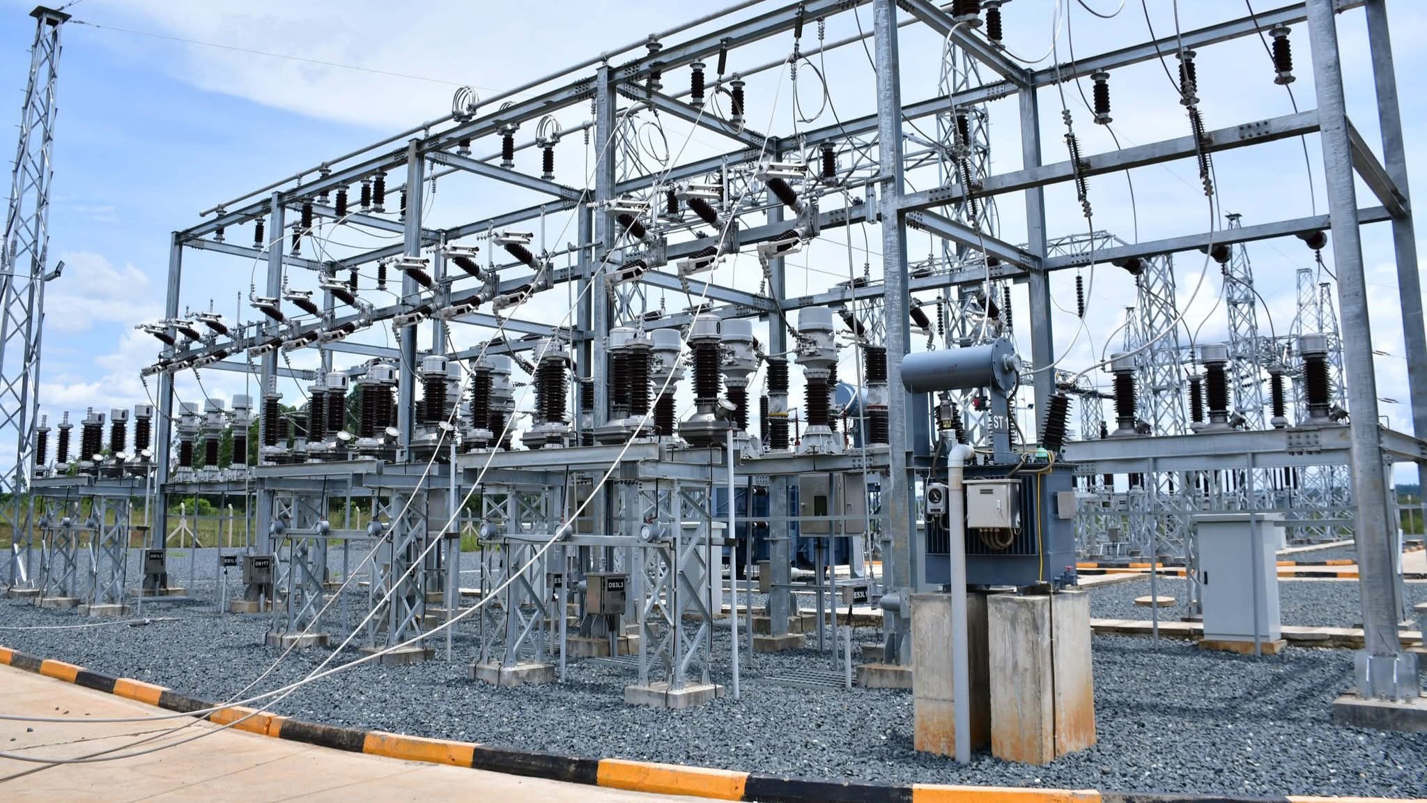 A high-voltage 132kV steel lattice transmission tower standing in a rural landscape, carrying power lines for the Sondu-Ndhiwa-Awendo project.