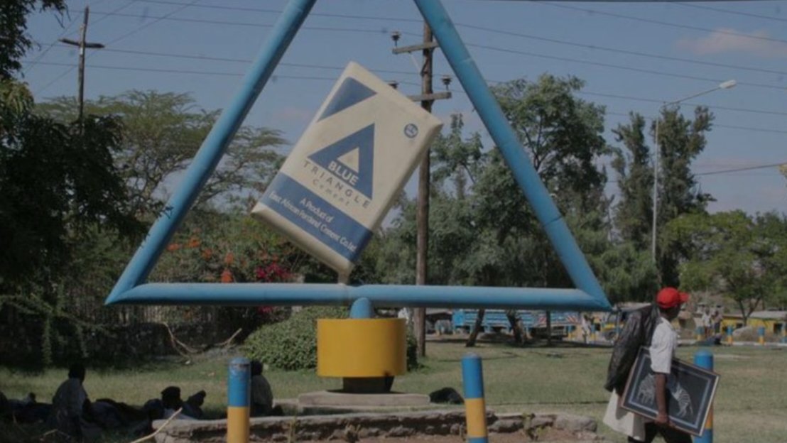 A Blue Triangle Cement brand sign mounted on a metal frame structure outside the East African Portland Cement manufacturing facility.
