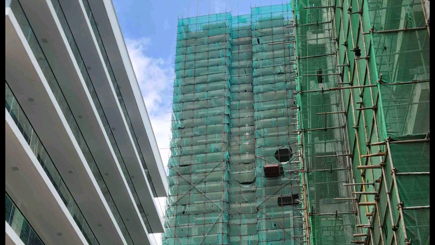 High-rise apartment building under construction in Nairobi, covered in green safety netting, situated next to an existing multi-story residential block.