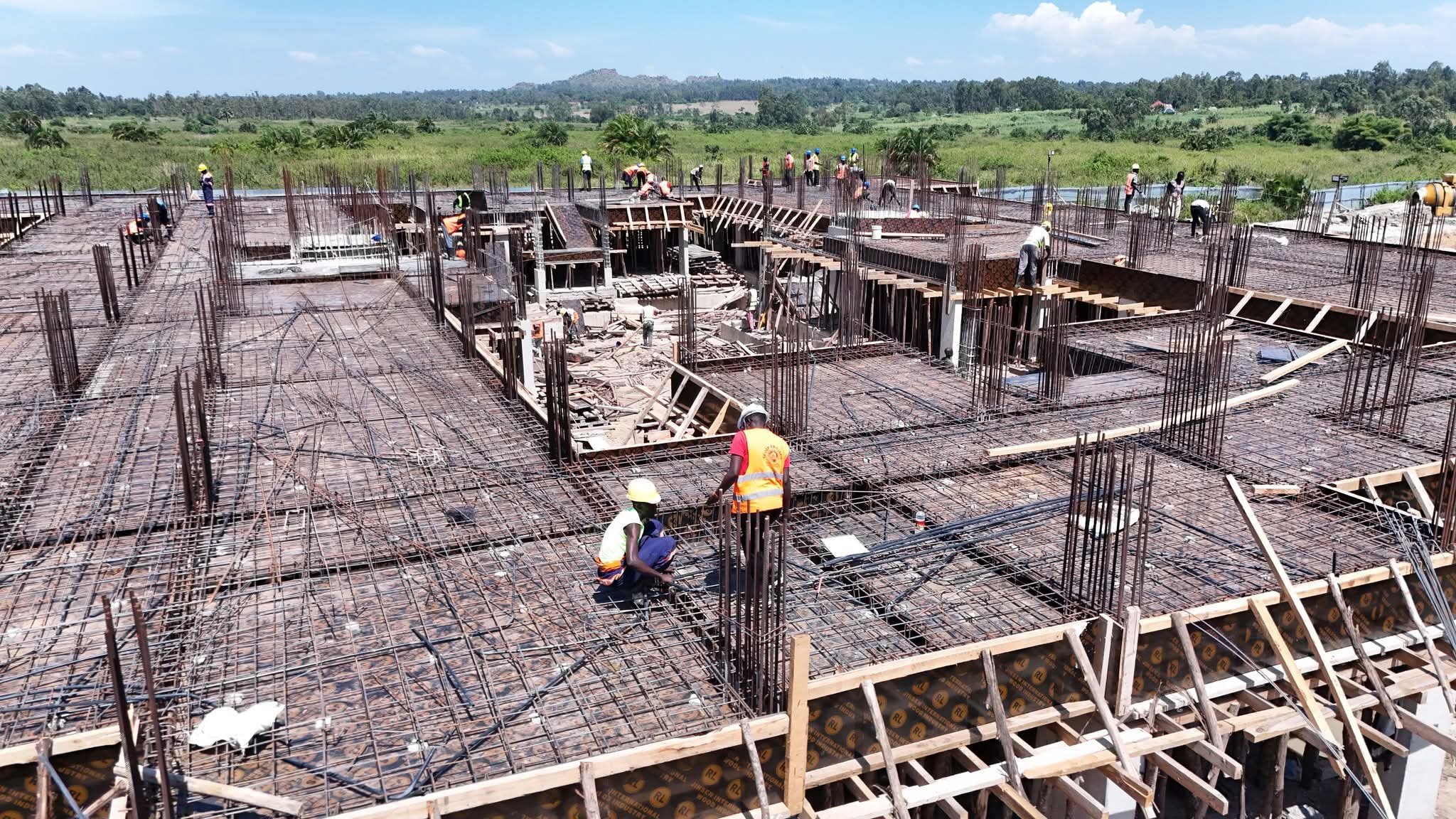A multi-story concrete structure under construction with scaffolding and a large workforce on-site at Alupe University.