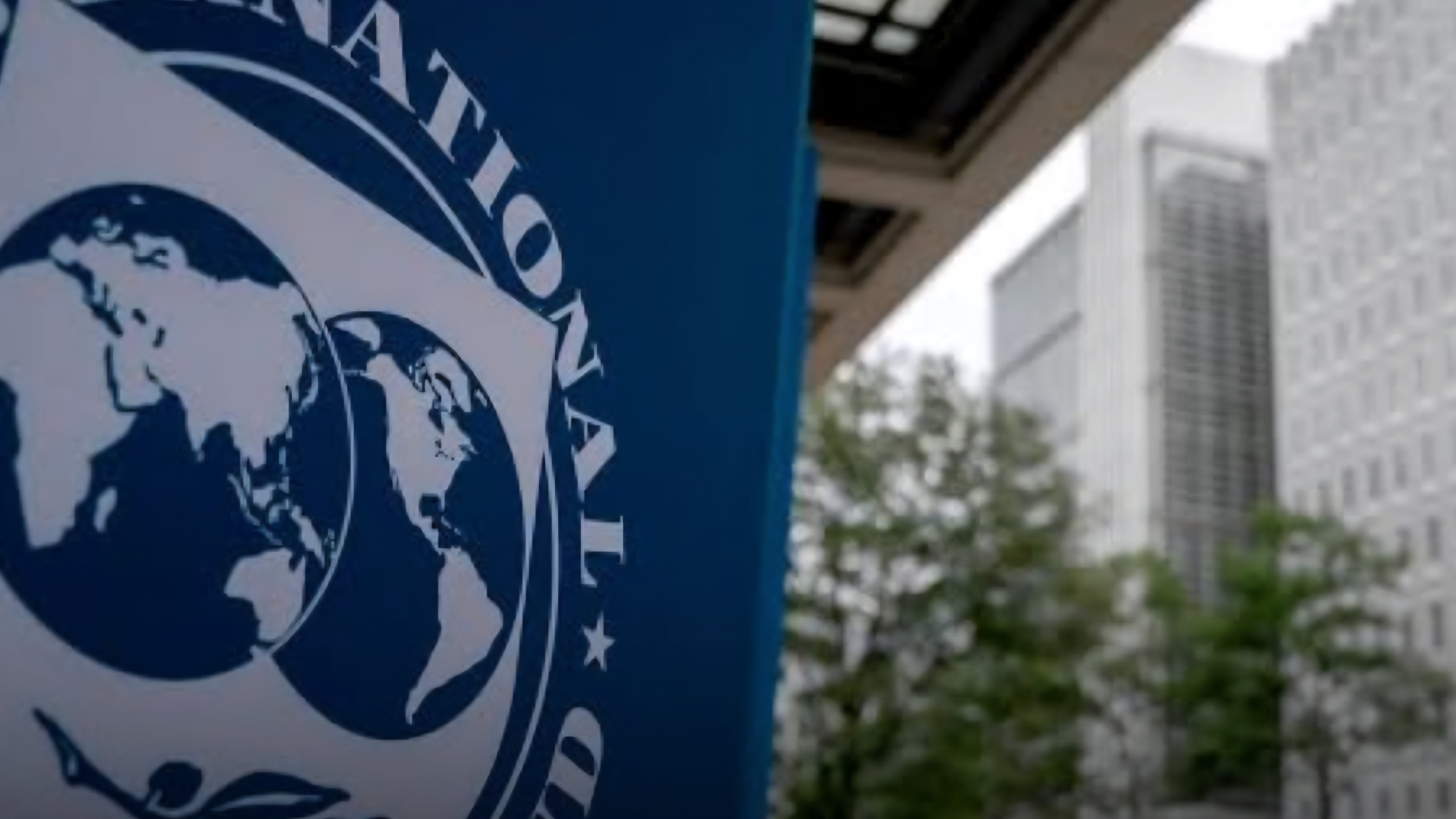 Close-up of the International Monetary Fund blue logo sign outside an office building facade.
