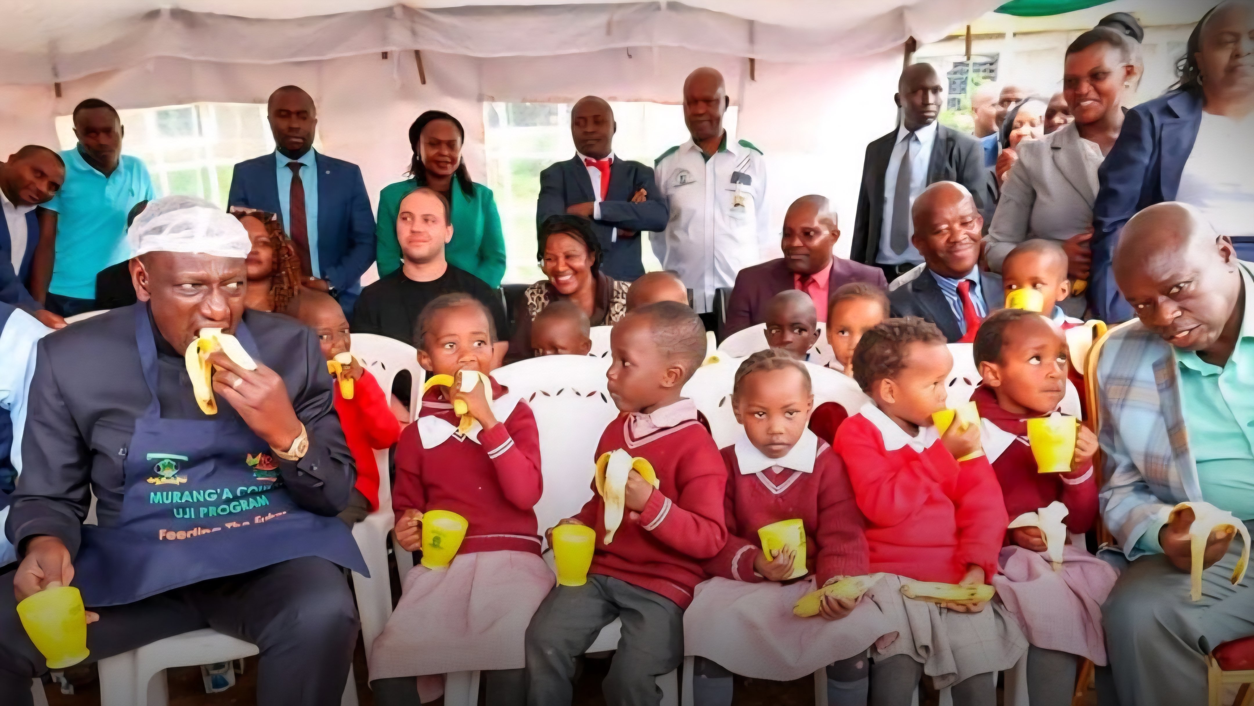 Governor Irungu Kang'ata sits with school children during a feeding program event in Murang'a County.