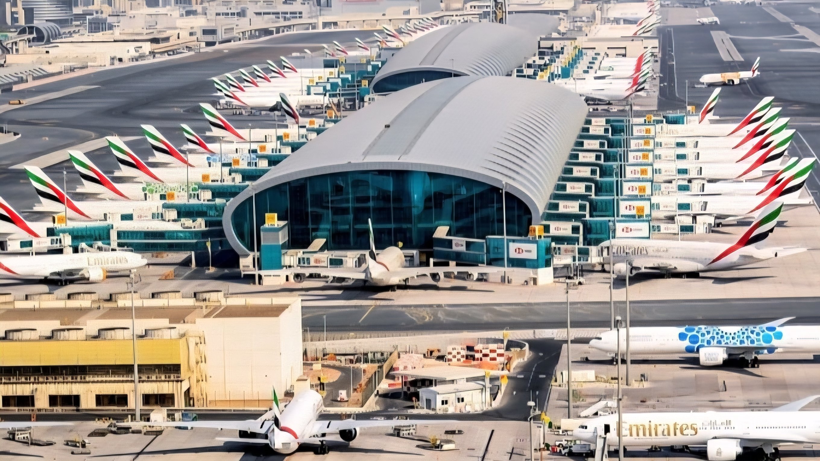 A wide view of the modern terminal exterior and control tower at Dubai International Airport with aircraft parked at gates.