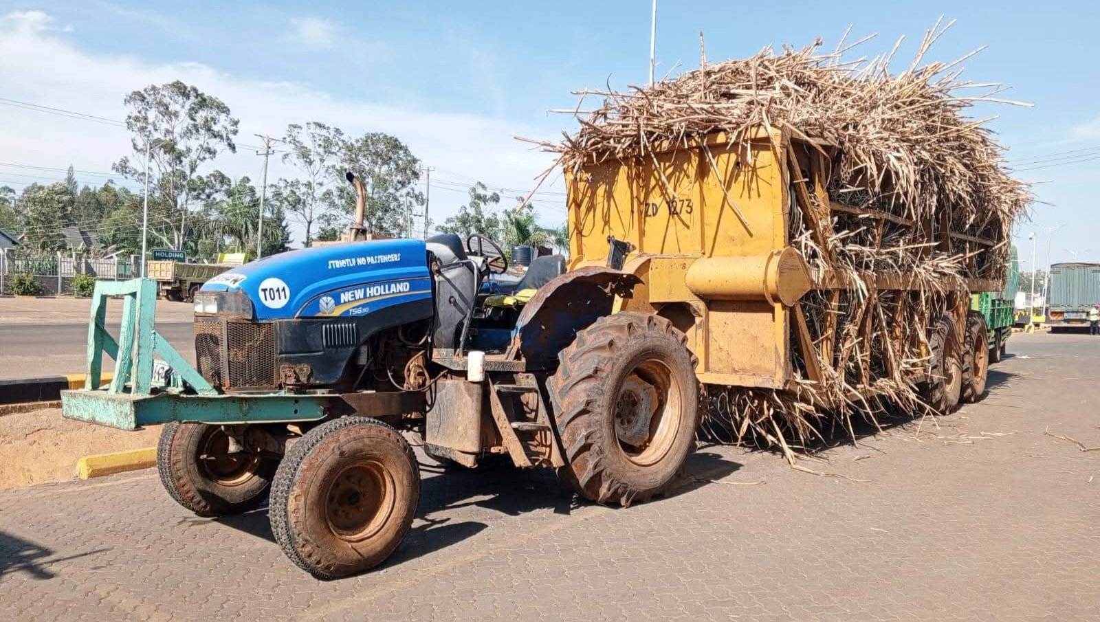 A tractor carrying an oversized load of sugarcane stopped by enforcement officers on a tarmac road in Kenya.