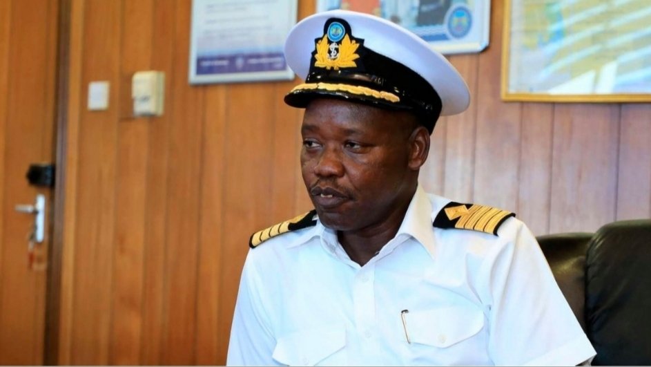 A woman wearing an apron pulls a heavy wooden cart loaded with sacks and supplies along a street.