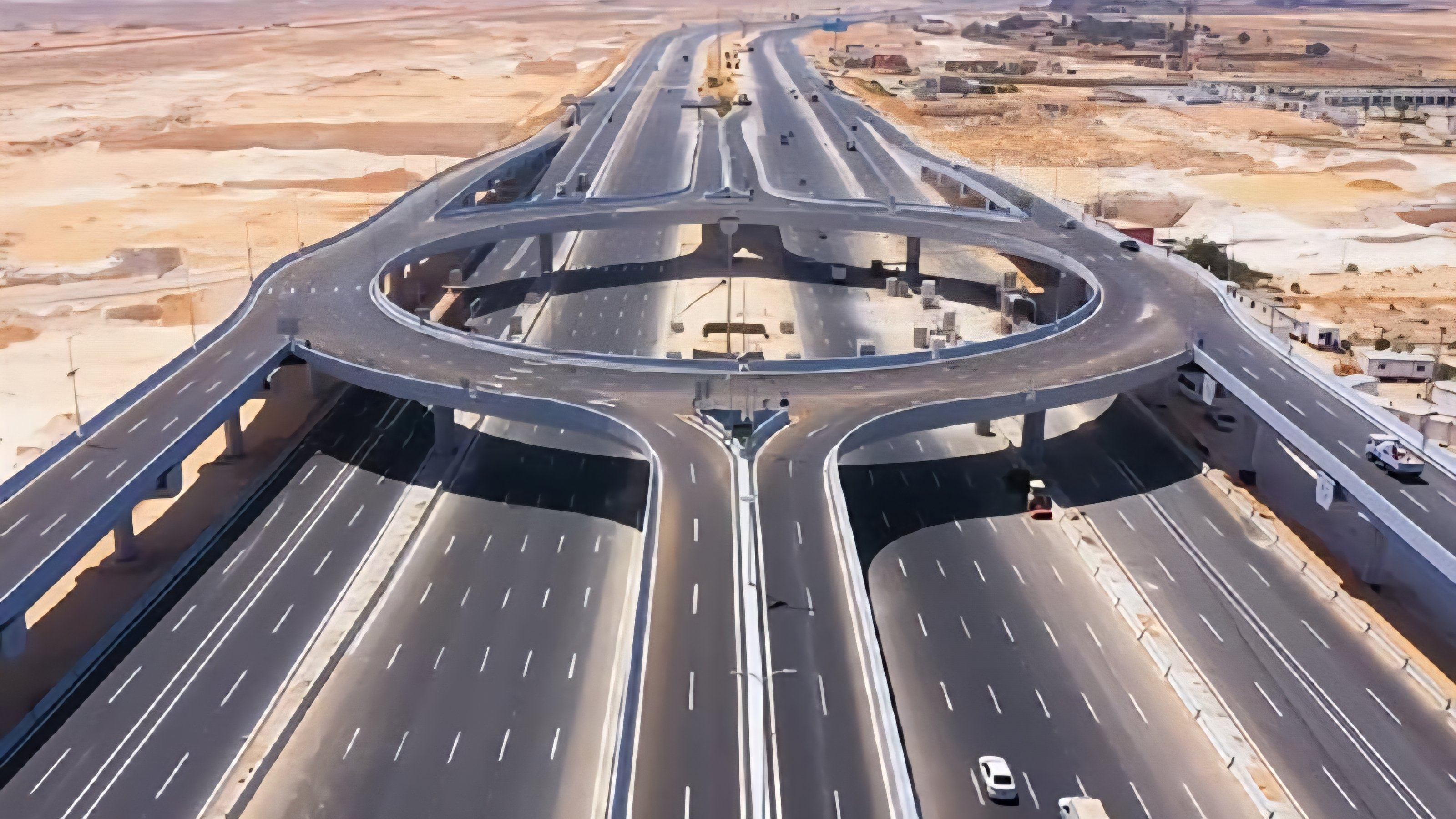 High-angle view of a modern multi-lane highway crossing through a desert landscape with a concrete overpass bridge.