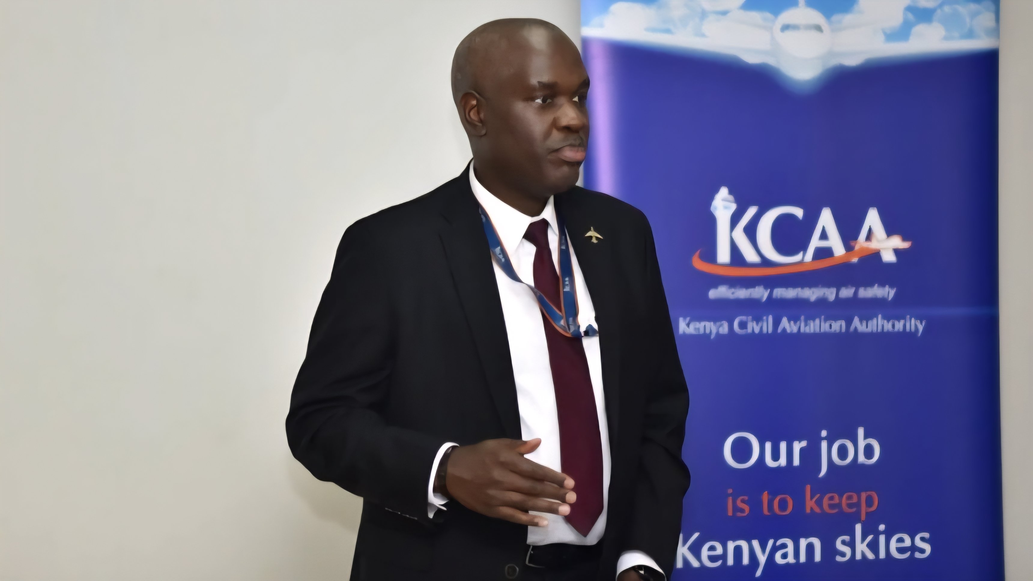 A formal portrait of the outgoing KCAA Director General Emile Arao standing before a Kenya Civil Aviation Authority banner.