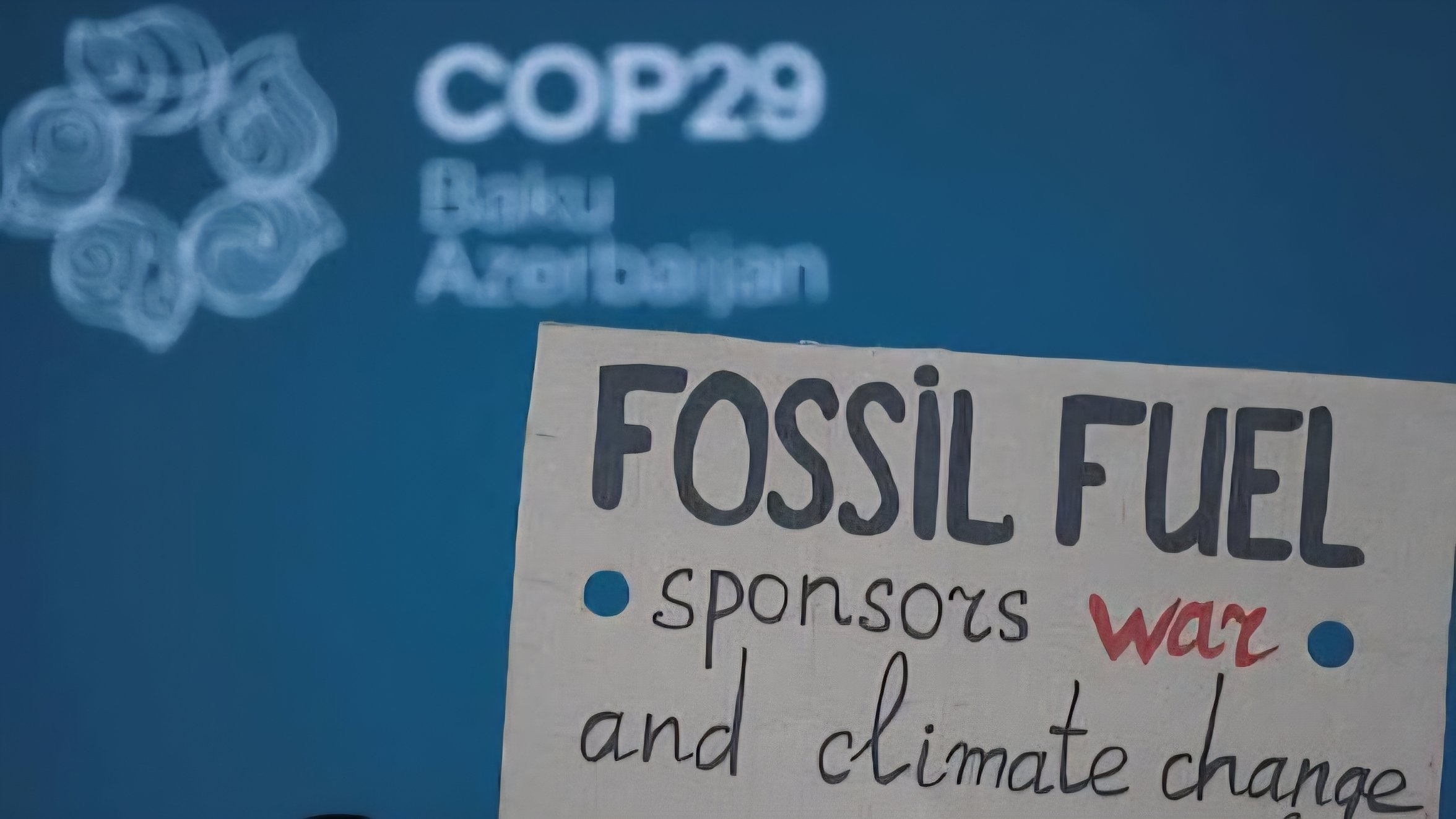 A protest sign at a climate event reading Fossil Fuel sponsors war and climate change with the COP29 Baku Azerbaijan logo in the background.