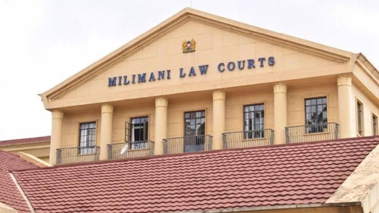 A low-angle view of the exterior facade of the Milimani Law Courts building in Nairobi, showing its prominent yellow columns and architectural entry.