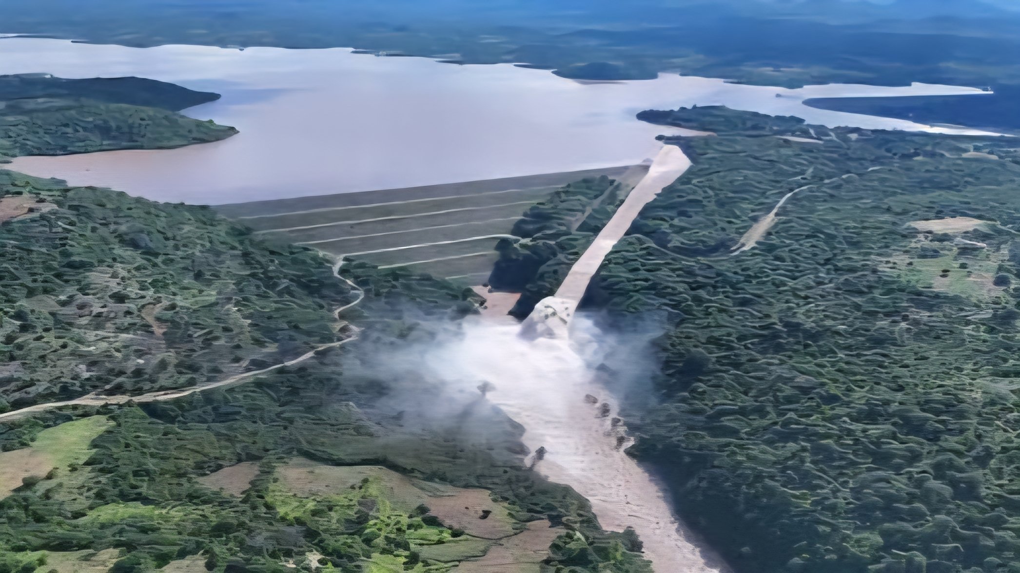 Aerial view of a large hydroelectric dam and reservoir surrounded by dense green forest in Kenya.