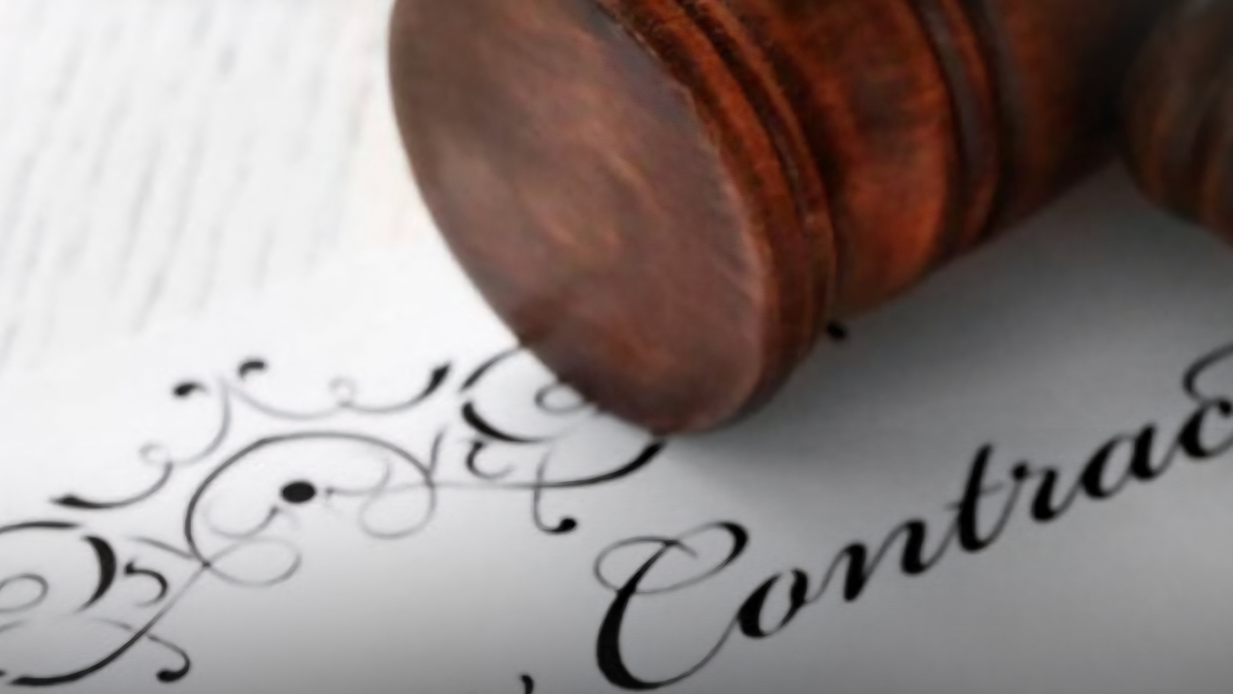 A wooden judge's gavel resting on legal documents alongside a pair of gold wedding rings.