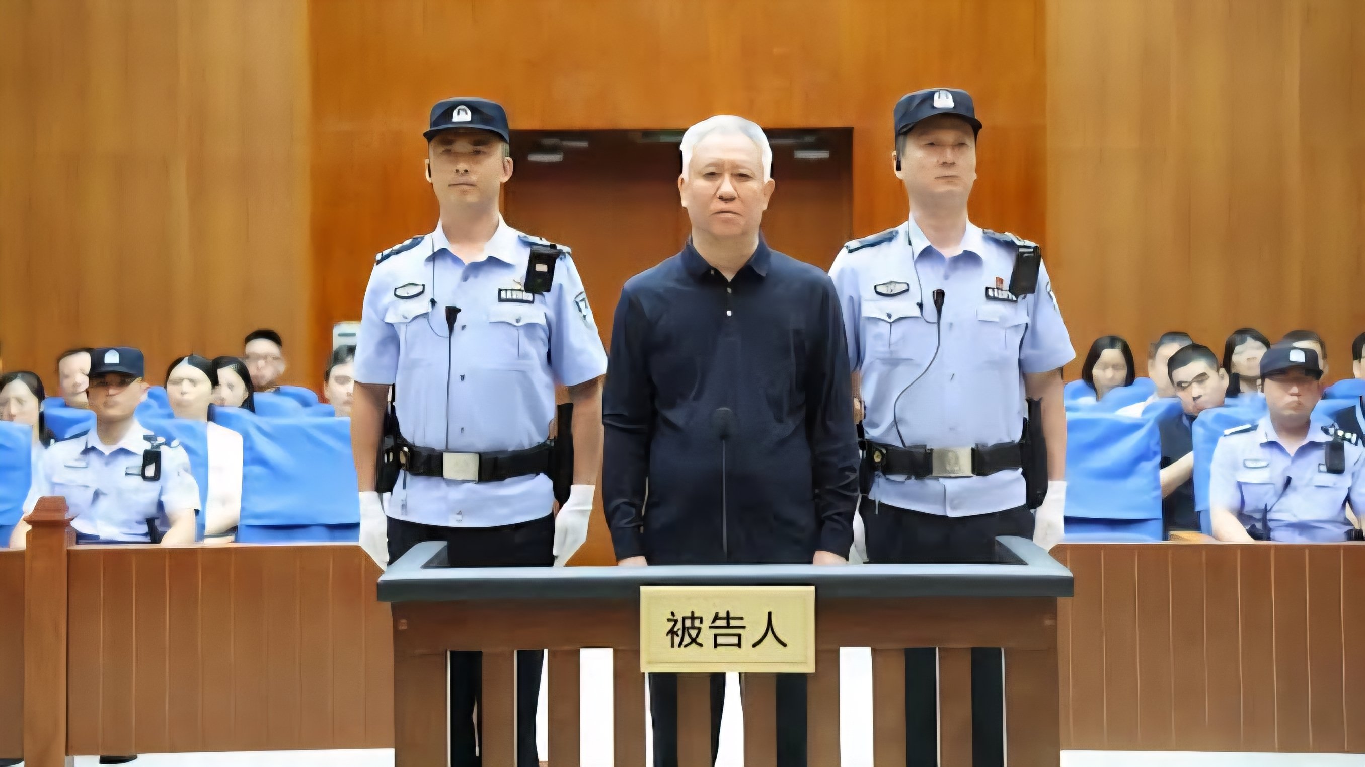 Evergrande founder Hui Ka Yan standing in a courtroom flanked by law enforcement officers during sentencing.