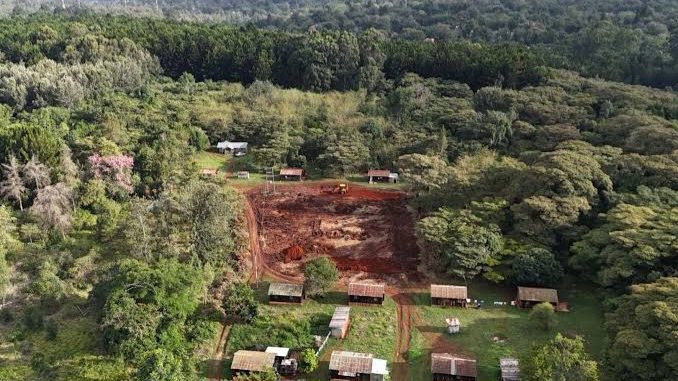 An aerial view of the dense canopy of Karura Forest in Nairobi with a cleared section of land where construction materials and temporary structures are visible.