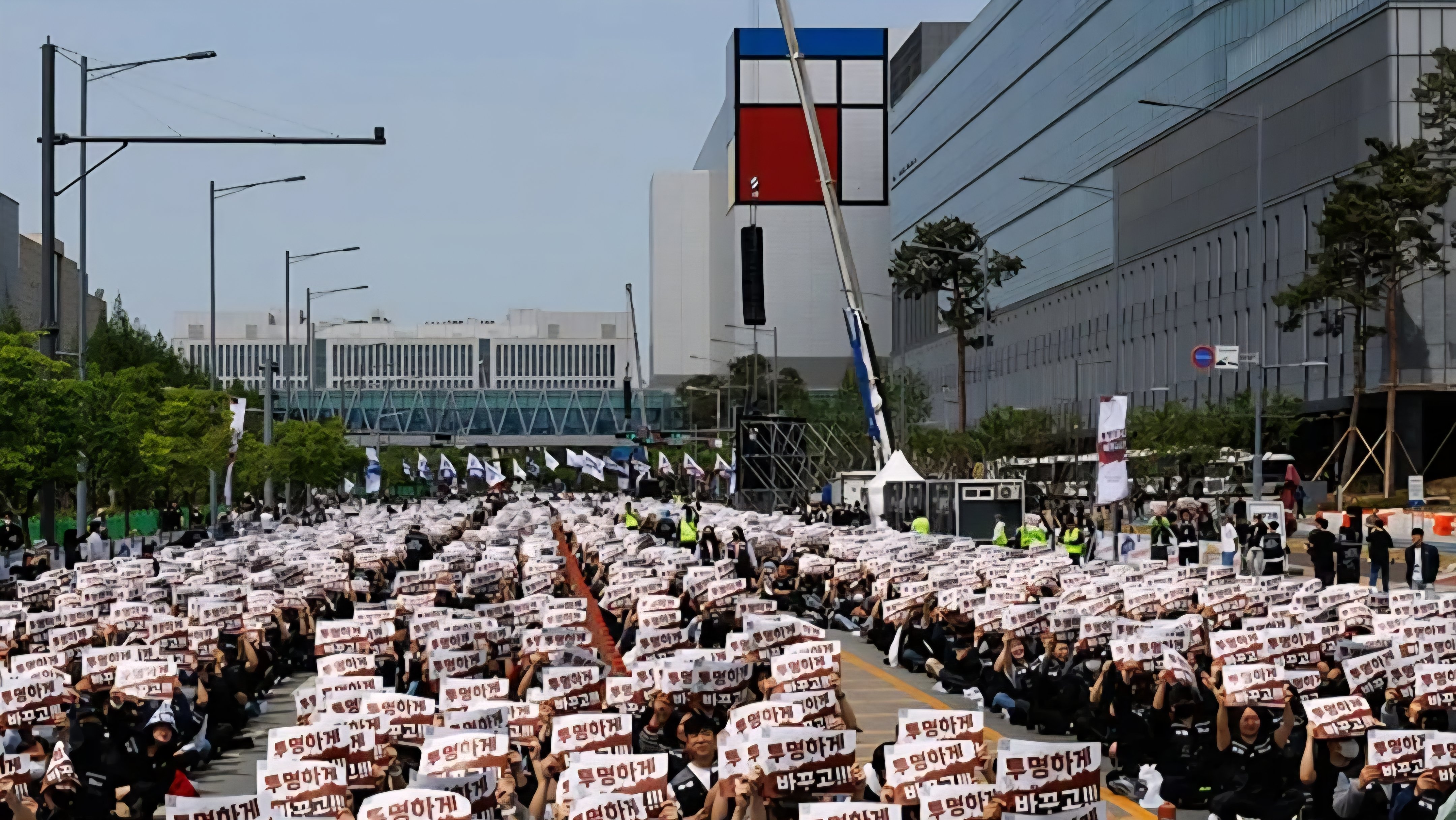 A crowded street filled with thousands of protesting Samsung Electronics labor union members wearing black shirts and holding up identical red and white signs during a demonstration in South Korea.