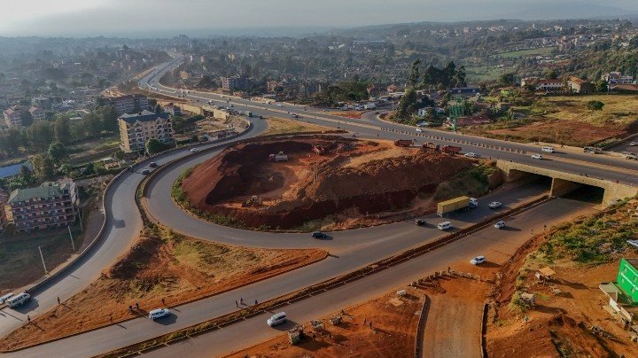 Heavy construction machines working on a newly built section of highway in northern Kenya, with road rollers and excavators laying tarmac along a wide, open landscape.