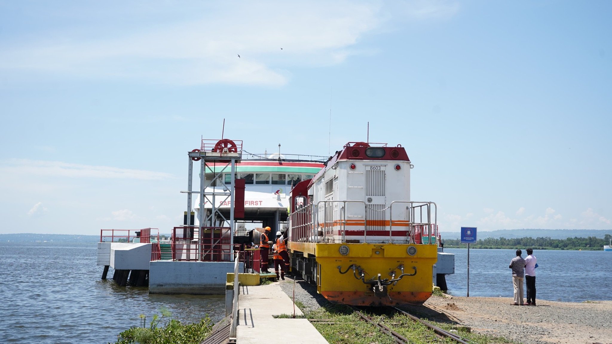 A locomotive engine positioned on a rail track leading onto a large white and red wagon ferry docked at a port under a clear sky.