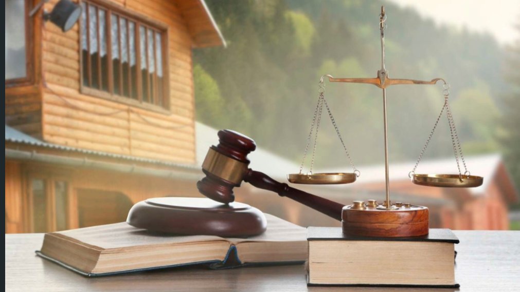 A judge wooden gavel and scales of justice resting on a wooden desk with a house in the background.